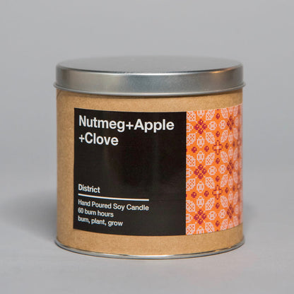 Hand poured soy candle with nutmeg, apple, and clove scent in a brown container with a metal lid and decorative label