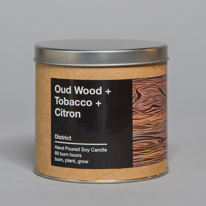 Hand-poured soy candle in metal tin featuring oud wood, tobacco, and citron scents with woodgrain label design