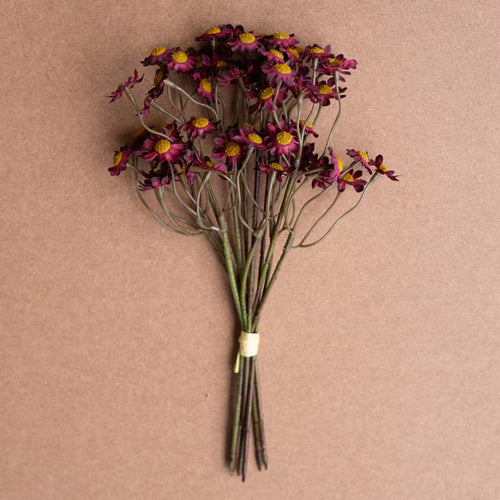Bundle of deep red faux chamomile flowers with yellow centers against a neutral brown background for home decor