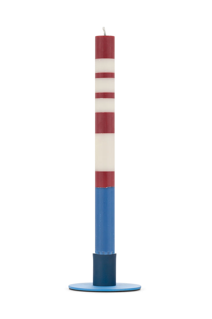 Tall striped candle with red, white, and blue colors on a simple round metal holder for home decor.