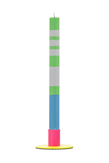 Tall colorful candle with green, white, blue, and pink sections on a yellow metal holder against a white background