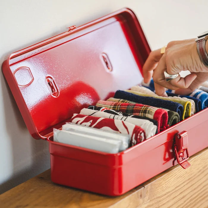 Hand selecting folded fabric pieces stored neatly inside an open red steel toolbox on a wooden surface