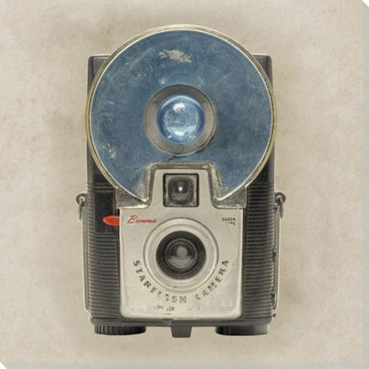 Close-up of a vintage camera with large circular flash, showcasing retro design and metal details on neutral background