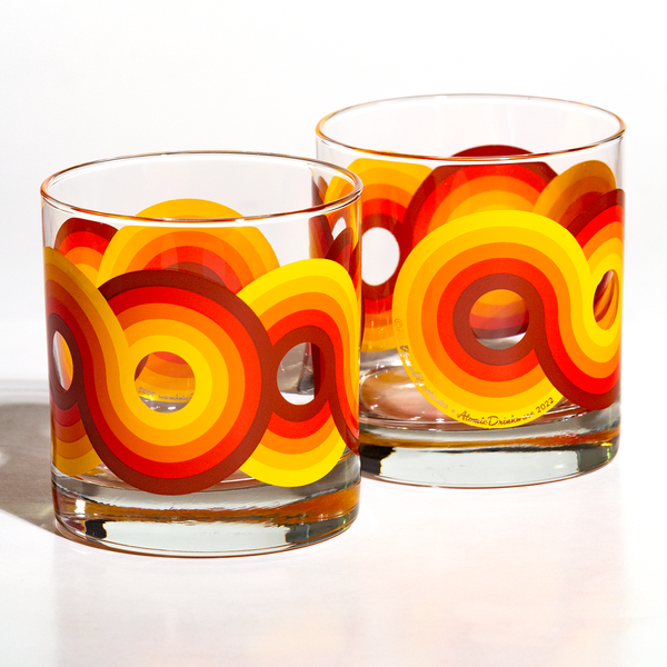Pair of clear glass rocks glasses with vibrant orange and yellow retro swirl patterns for stylish home decor.